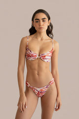 A woman modeling a two-piece bikini swimsuit with a red, orange, and white abstract pattern against a plain light beige background.